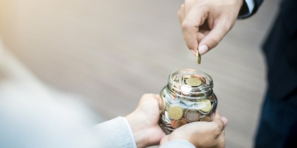 Businessman hand putting money (coin) in the glass jar held by a woman