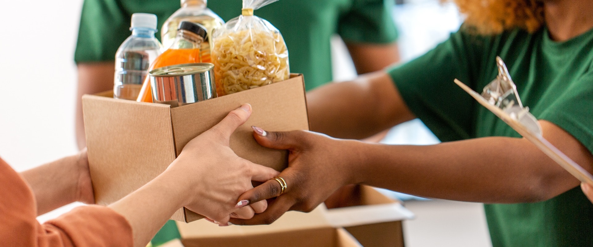 charity, donation and volunteering concept - close up of volunteers giving box of food at distribution or refugee assistance center