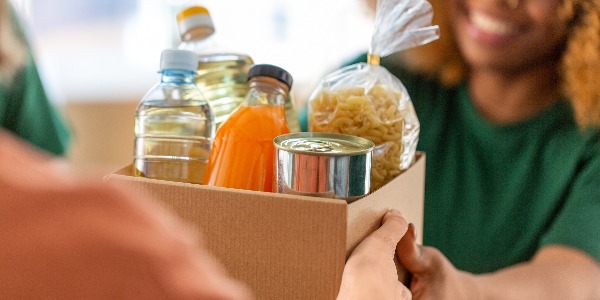 charity, donation and volunteering concept - close up of volunteers giving box of food at distribution or refugee assistance center